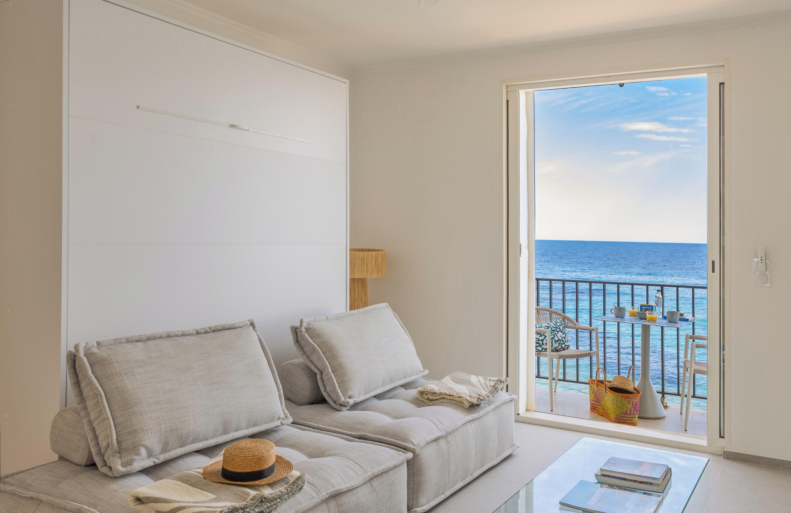 A room with a sofa, a table, and a view of the sea through a balcony.