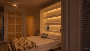 Une chambre à coucher comprenant un lit, un ventilateur de plafond, une table de chevet et une étagère fixée au mur avec un livre.