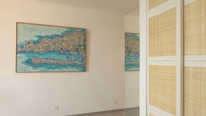 Une pièce dans laquelle on trouve une grande œuvre d’art encadrée au mur, un miroir qui reflète une partie de la pièce et un panneau mural à motifs.