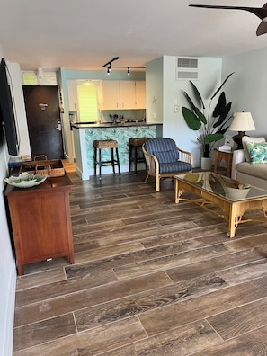 A living room with a sofa, coffee table, and chairs, a kitchen with a counter and cabinets, and a door with a handle. - Ka'anapali Condo · Pool View Lanai · Black Rock Beach · Maui Eldorado C202 (Lahaina)