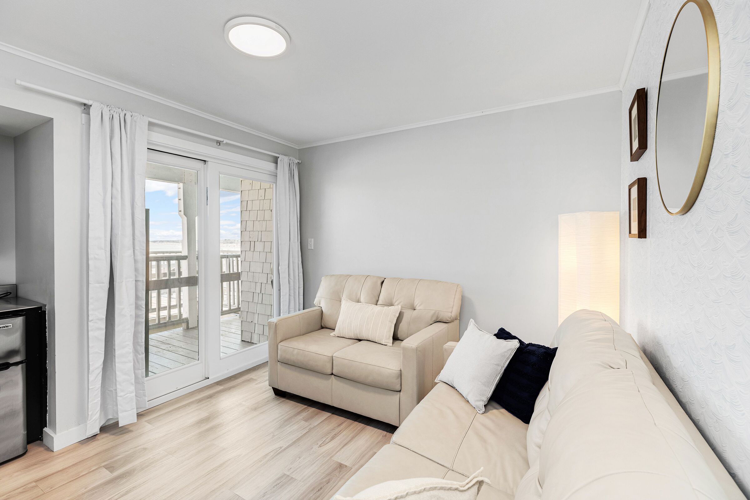 Ein Wohnzimmer mit einem beigen Sofa, einem kleinen Tisch und einer Schiebeglastür, die auf einen Außenbalkon führt.