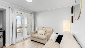 Ein Wohnzimmer mit einem beigen Sofa, einem kleinen Tisch und einer Schiebeglastür, die auf einen Außenbalkon führt.