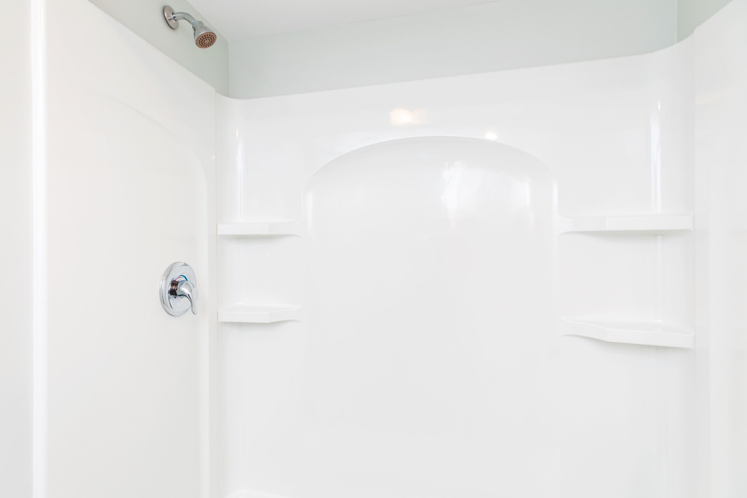 A white, empty bathroom with a shower, a toilet, and a sink.