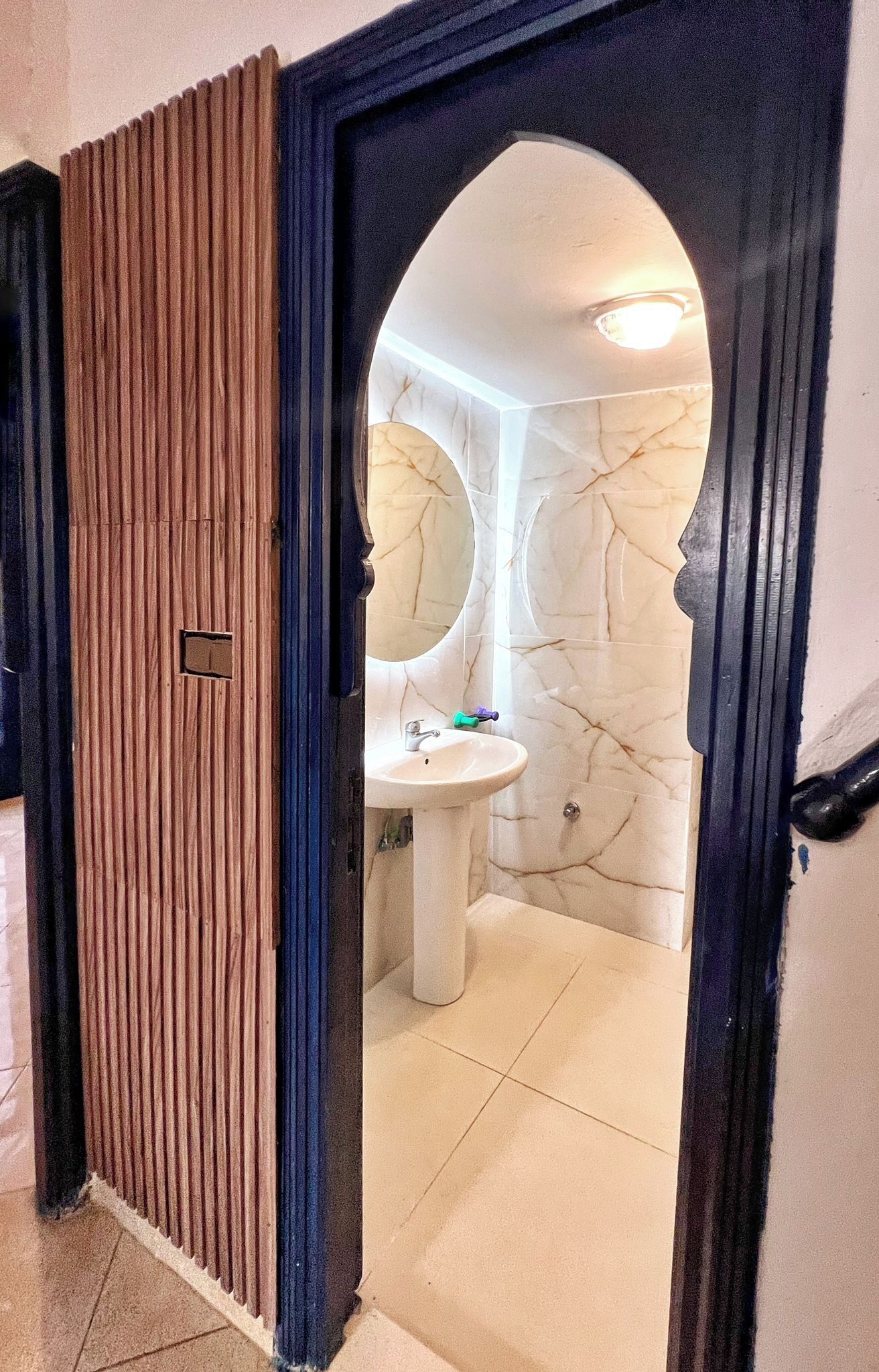 A bathroom with a marble wall, a sink, and a mirror.
