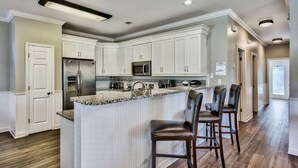 Een moderne keuken met witte kasten, een centraal kookeiland met barstoelen, roestvrijstalen apparatuur en een granieten aanrecht.
