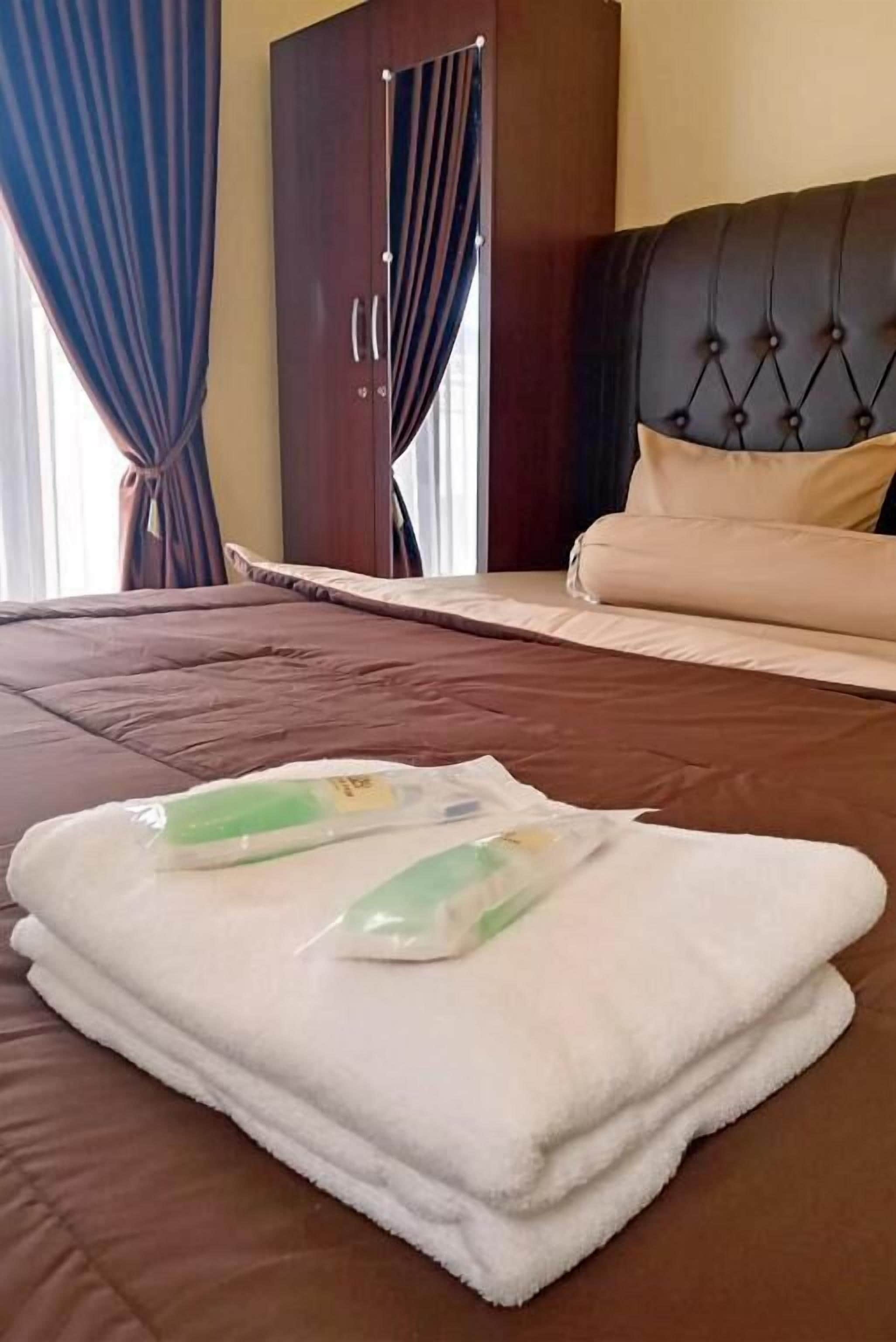 A neatly made bed with a brown cover, a white towel, and two green bottles on it.