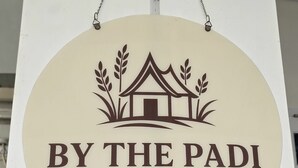 A circular sign with a house and wheat graphic, labeled 'BY THE PADI HOMESTAY.' - By The Padi - Homestay (Padang)