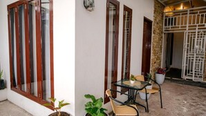 A patio area with a table and chairs, potted plants, and a brick wall. - By The Padi - Homestay (Padang)