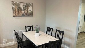 Ein Essbereich mit einem rechteckigen Tisch, sechs Stühlen, einer Topfpflanze und einem gerahmten Bild an der Wand.