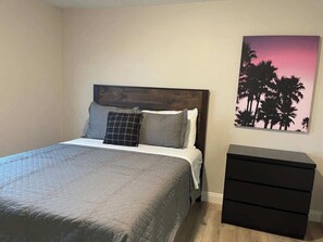 A bedroom with a bed, a dresser, and a wall with a sunset painting. - Charming & Chic: Your Stylish Oasis for a Month-Long Retreat (Henderson)
