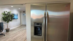 Ein Edelstahl-Kühlschrank mit Wasserspender in einer modernen Küche mit Holzboden und einer Topfpflanze.