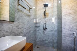 Une salle de bain avec un mur en marbre, une douche, un lavabo et un tabouret en bois.