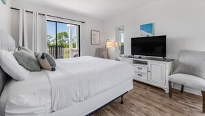 Un dormitorio con cama, televisor, una silla y vistas al balcón.