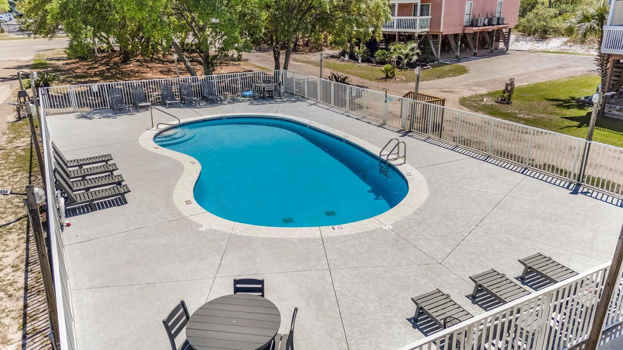 Uma piscina com borda curva, cercada por uma grade, adjacente a um edifício com varanda.