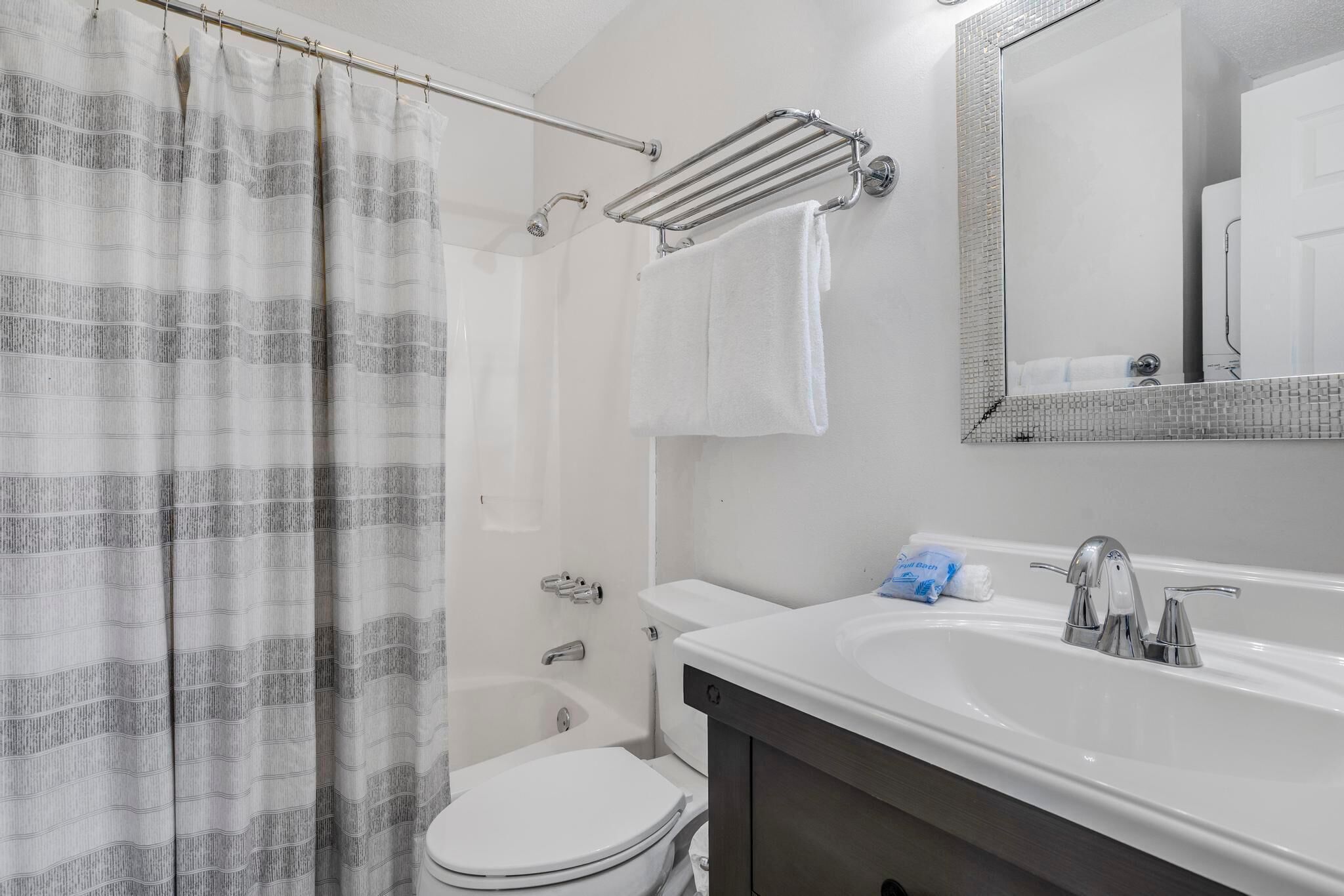 Une salle de bain avec un rideau de douche, des toilettes, un lavabo avec un miroir et un porte-serviettes.