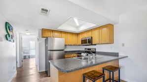 Cocina con armarios de madera, refrigerador de acero inoxidable, microondas y una isla con cubierta de granito y dos taburetes.