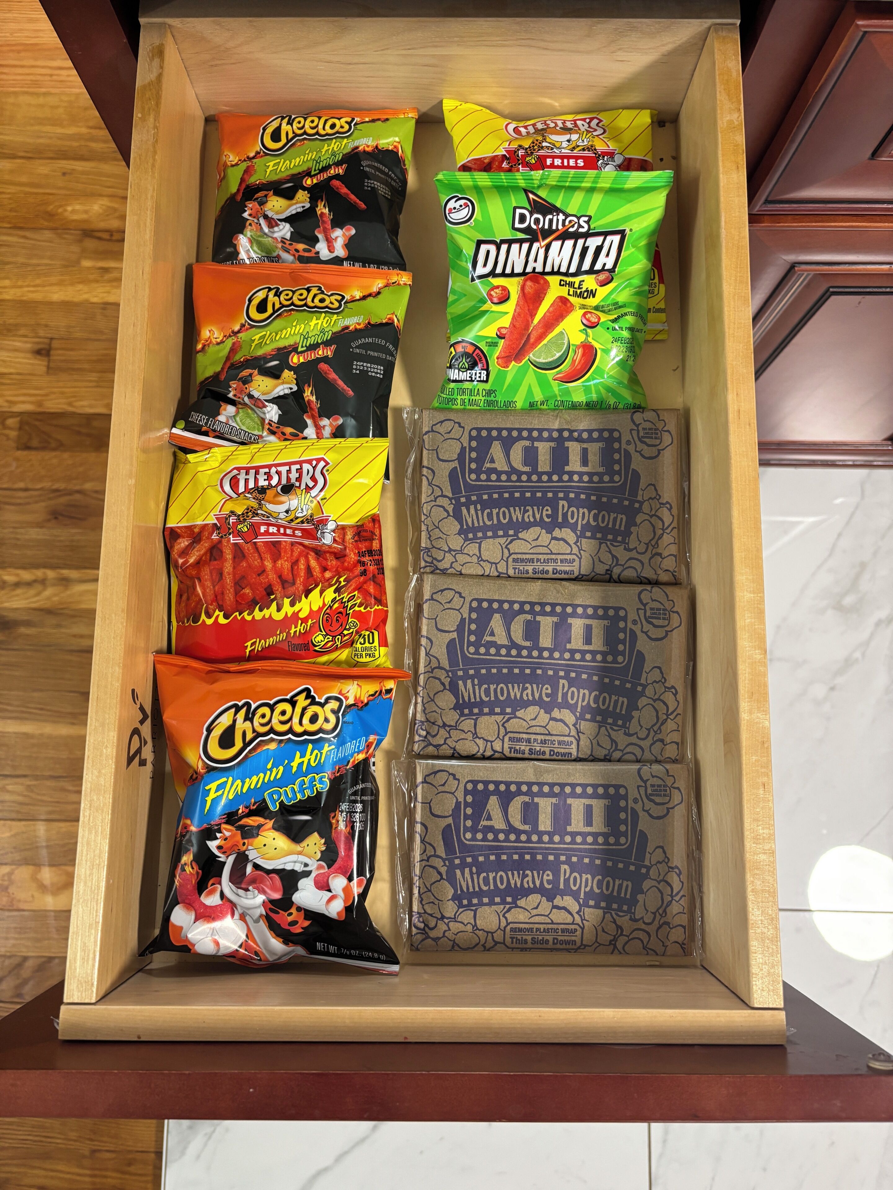 Eine Holzkassette mit verschiedenen Snacks, darunter Tüten Cheetos, Doritos und Mikrowellen-Popcorn.