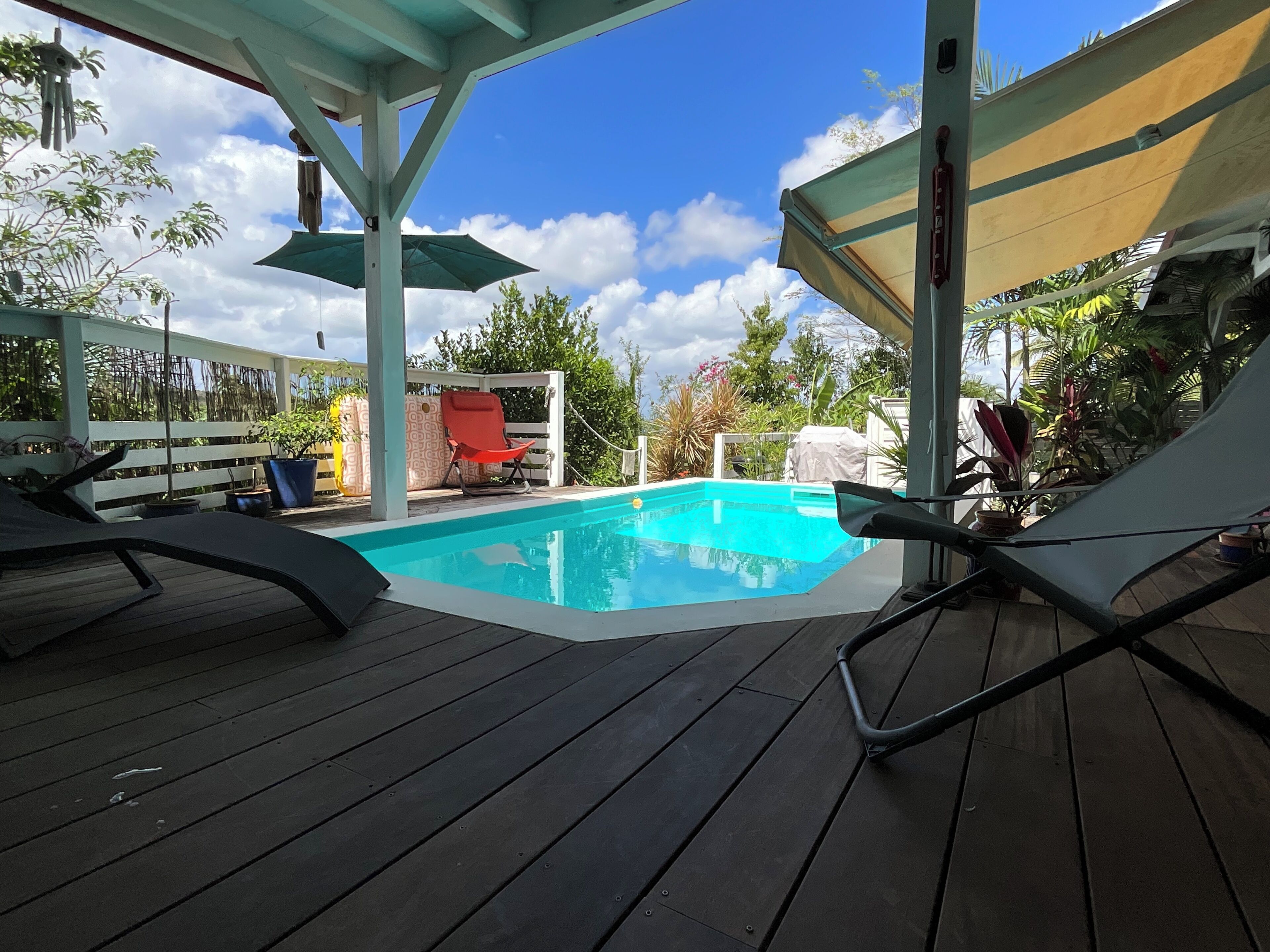 Uma área de piscina com deck de madeira, espaço coberto para sentar e uma cadeira vermelha.