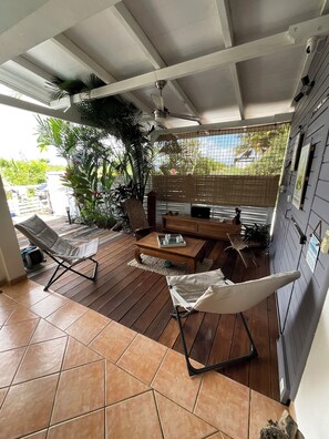 A covered patio area with wooden flooring, a ceiling fan, and a seating arrangement including a lounge chair and a cushioned chair. - Villa Colibri - Private Pool - Panoramic View (Rivière-Salée)