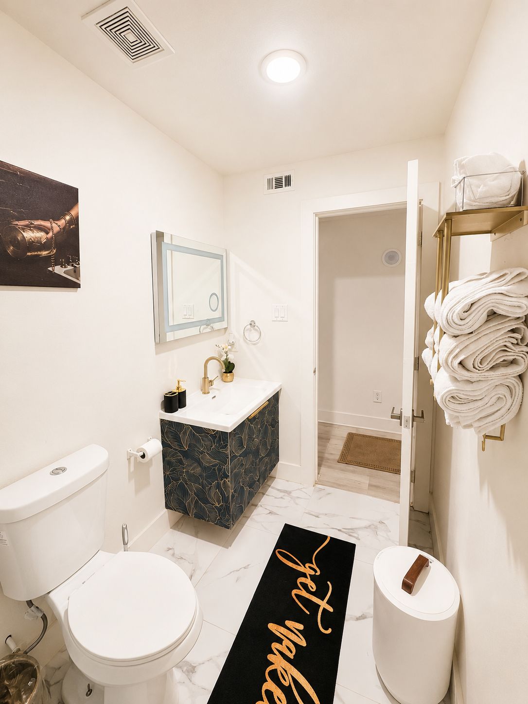 A modern bathroom with a white toilet, a vanity with a dark patterned sink, a mirror, and a towel rack.