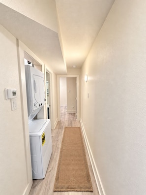 A laundry room with a washing machine and dryer, a hallway with a rug, and a door leading to another room.