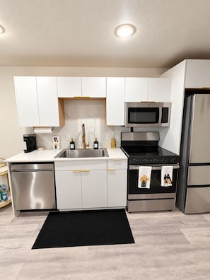 A modern kitchen with white cabinets, stainless steel appliances, and a black rug.
