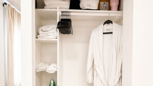 A white closet with shelves, a hanging robe, and a laundry basket. - Elegant Downtown Dallas Retreat (Dallas)