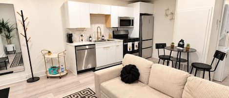 Un apartamento moderno con kitchenette, un conjunto de sofás, zona de comedor y una pequeña mesa con sillas.