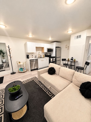 A modern apartment with a kitchenette, a sofa set, a dining area, and a small table with chairs.