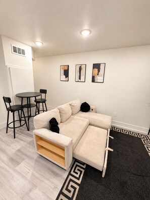 A modern living room with a sectional sofa, a round dining table, and three framed artworks on the wall.