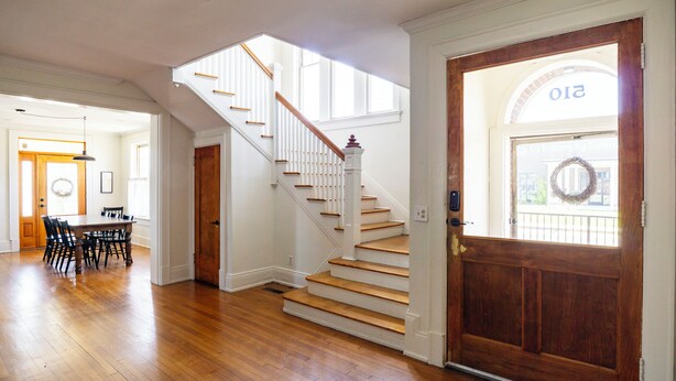 A spacious interior with a wooden staircase, a dining area, and a front door with a sign. - Historic 1915 Home · No Pet Fees (Chattanooga)
