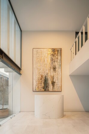 Un interior moderno con un cuadro abstracto grande, un banco de mármol y una barandilla de vidrio.
