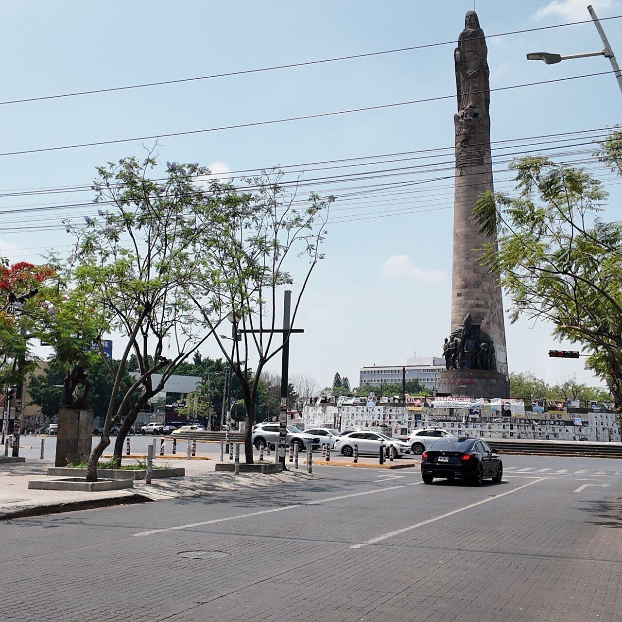 A tall monument with a statue base, surrounded by trees and a busy street with cars.