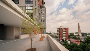 A rooftop terrace with potted plants, a view of the cityscape, and a tall monument. - CONCORDIA CHAPULTEPEC (Guadalajara)