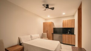 A bedroom with a bed, nightstand, chair, wooden wardrobe, and a kitchenette with a sink. - CONCORDIA CHAPULTEPEC (Guadalajara)
