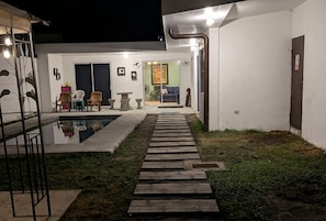 Un espace extérieur moderne doté d’une piscine, de coins salon et d’un chemin dégagé menant à l’entrée d’un bâtiment.