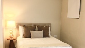 Una camera da letto con un letto, un comodino con una lampada e un punto luce a parete.