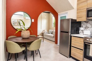 A modern kitchen with a stainless steel refrigerator, a coffee maker, and a microwave. There is a dining area with a round table and chairs. - Cozy 2 Br Apartment Steps from La Cerra (San Juan)