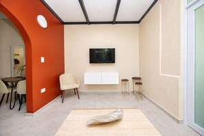 A modern interior with a dining area, a sofa, a TV mounted on the wall, and a small table with stools. - Cozy 2 Br Apartment Steps from La Cerra (San Juan)