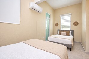 A bedroom with two beds, a window with blinds, an air conditioning unit, and a door. - Cozy 2 Br Apartment Steps from La Cerra (San Juan)
