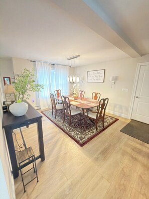 Un coin repas avec une table et des chaises en bois, un vase avec des feuilles vertes, un tapis et un mur orné d’une citation encadrée.
