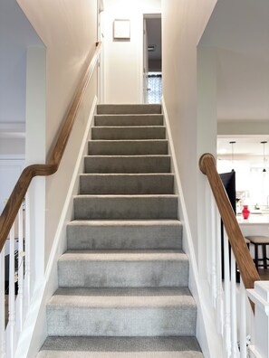 Una escalera con barandilla de madera, peldaños alfombrados y paredes blancas.