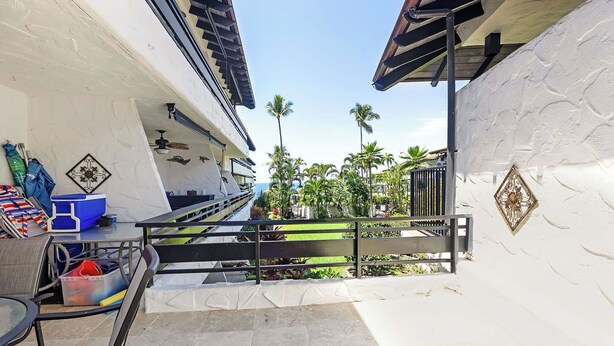 A balcony with a view of palm trees and a building. - Ocean View Condo with Lanai, Pools in Kailua-Kona (Kailua Kona)