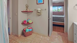 Ein Badezimmer mit Dusche, Handtuchhalter, Ablage für Toilettenartikel, einem Korb und einem Bett im angrenzenden Raum.