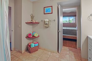 Ein Badezimmer mit Dusche, Handtuchhalter, Ablage für Toilettenartikel, einem Korb und einem Bett im angrenzenden Raum.