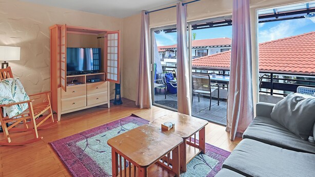Ein Wohnzimmer mit Holztisch, einer Couch, einem Fernseher und einer Schiebeglastür zum Garten.