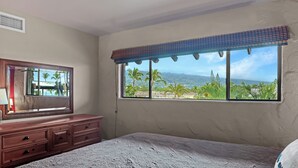 Ein Schlafzimmer mit einem großen Fenster, einer hölzernen Kommode und einem Bett.