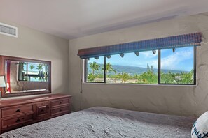 Ein Schlafzimmer mit einem großen Fenster, einer hölzernen Kommode und einem Bett.