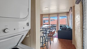 Ein kleiner Raum mit Waschmaschine, Essbereich mit Stühlen, Sofa und Blick auf Gebäude durch große Fenster.