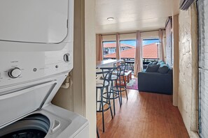 Ein kleiner Raum mit Waschmaschine, Essbereich mit Stühlen, Sofa und Blick auf Gebäude durch große Fenster.